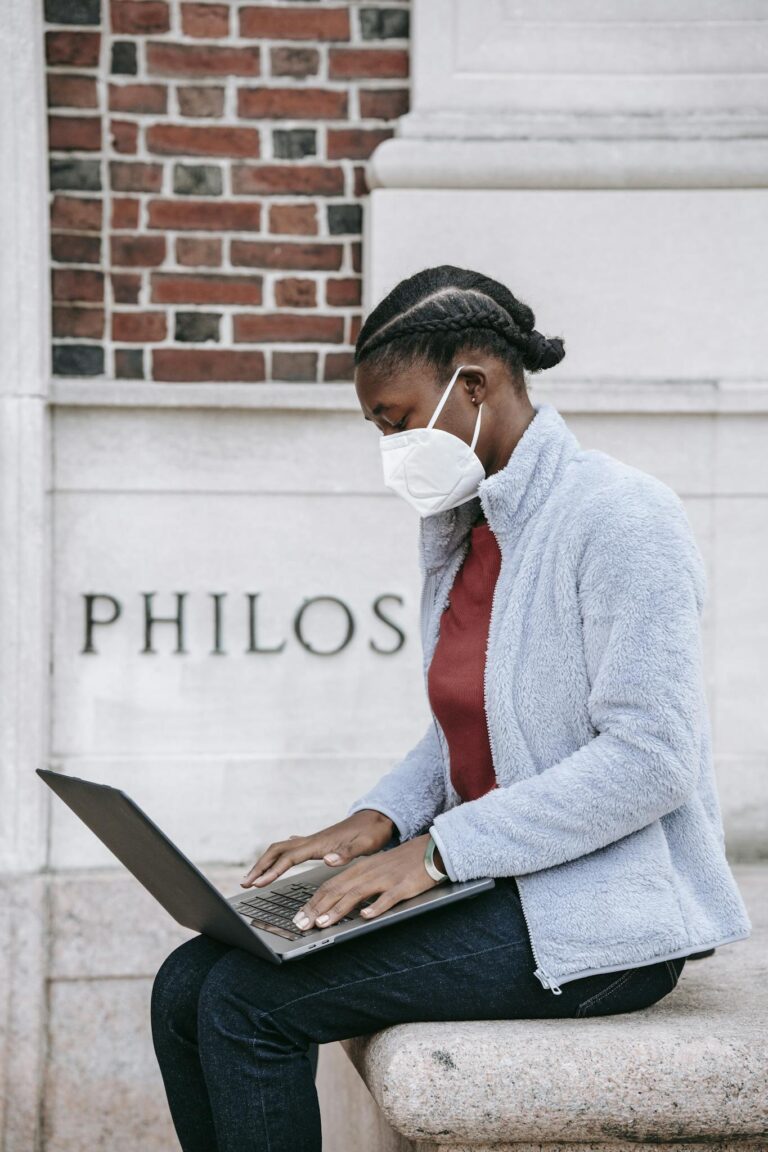 Young ethnic female student working on netbook near university building